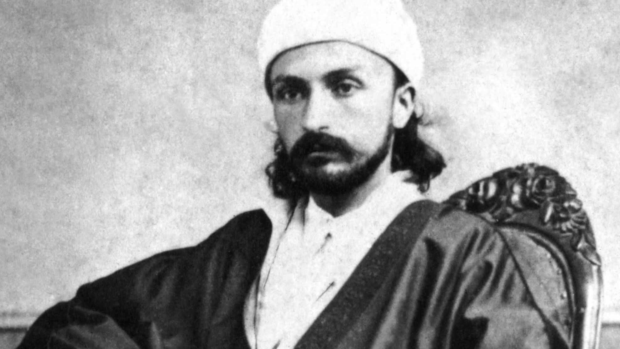 ‘Abdu’l-Bahá, as a young man, seated in a chair for an official portrait