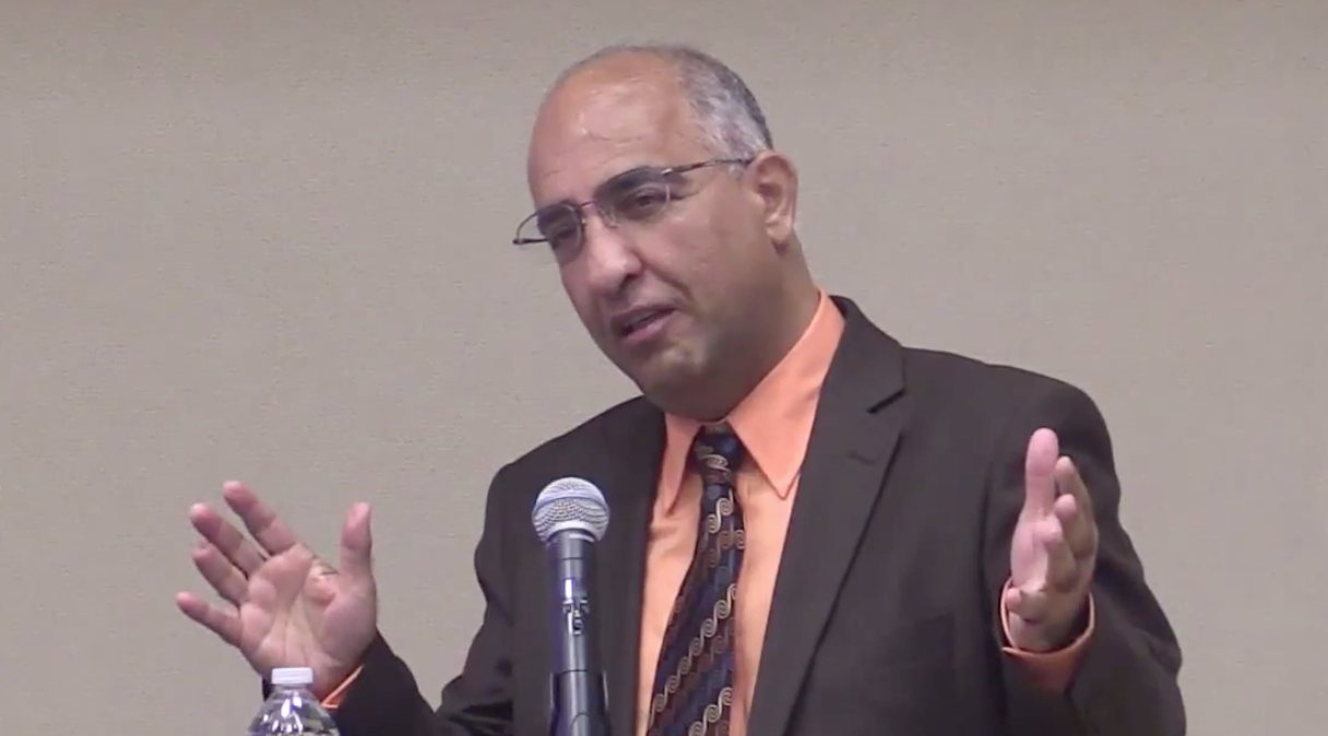 Habib Riazati speaking at a lectern and gestering animatedly with both hands