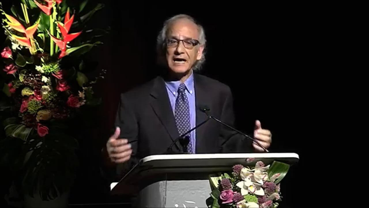 Nader Saiedi talks at a lectern where boquets of flowers are arranged