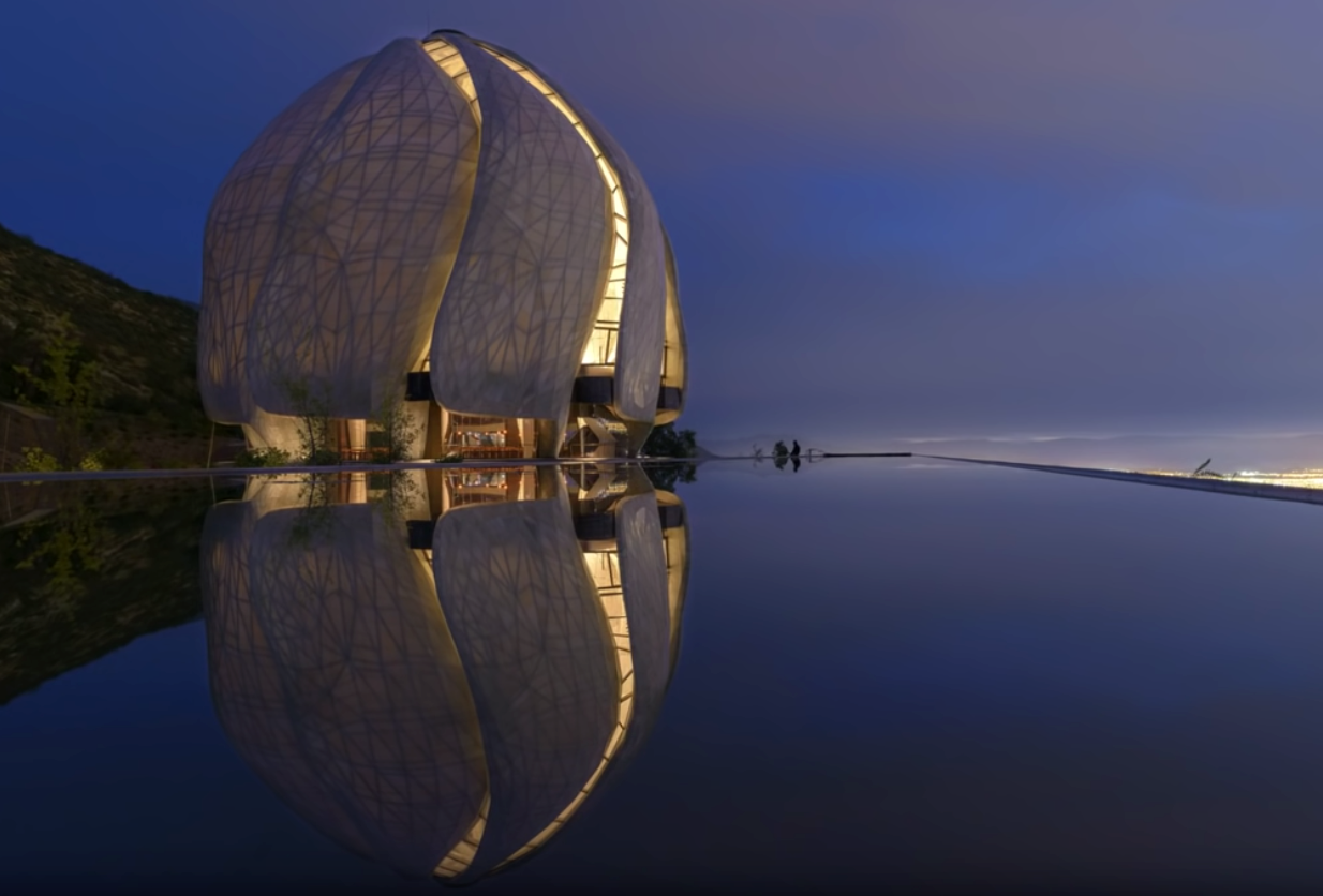a perfectly still pool of water reflects the Bahá’í Temple in Santiago Chile, an beautiful building of soft white alabaster in the shape of flower petals or sails